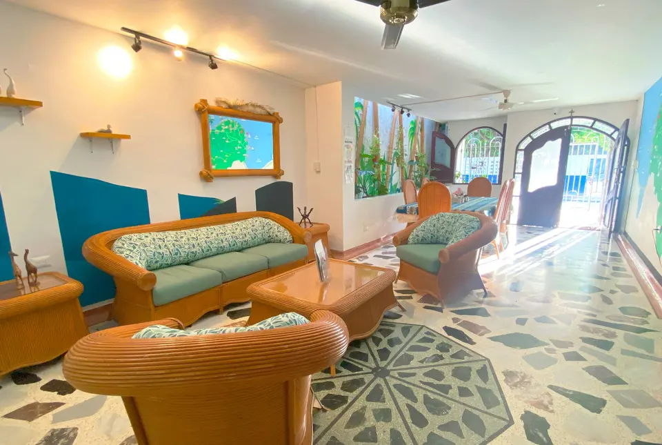 La sala a lo largo: muebles de mimbre, detalles turquesa en la pared, terrazo con una estrella en el piso y la puerta en arco al fondo
